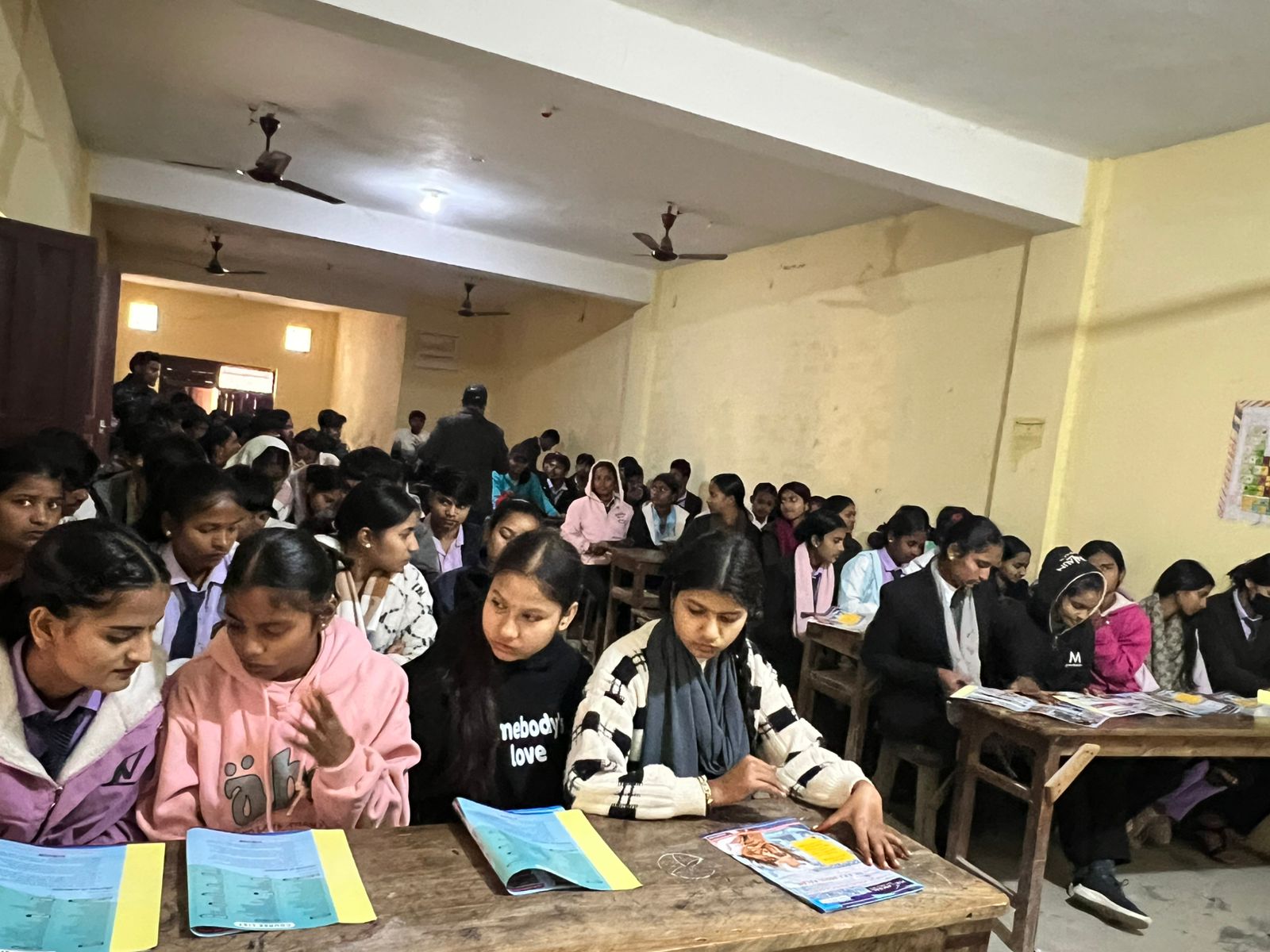Densely packed classroom — many students reading Mission Prayas booklets