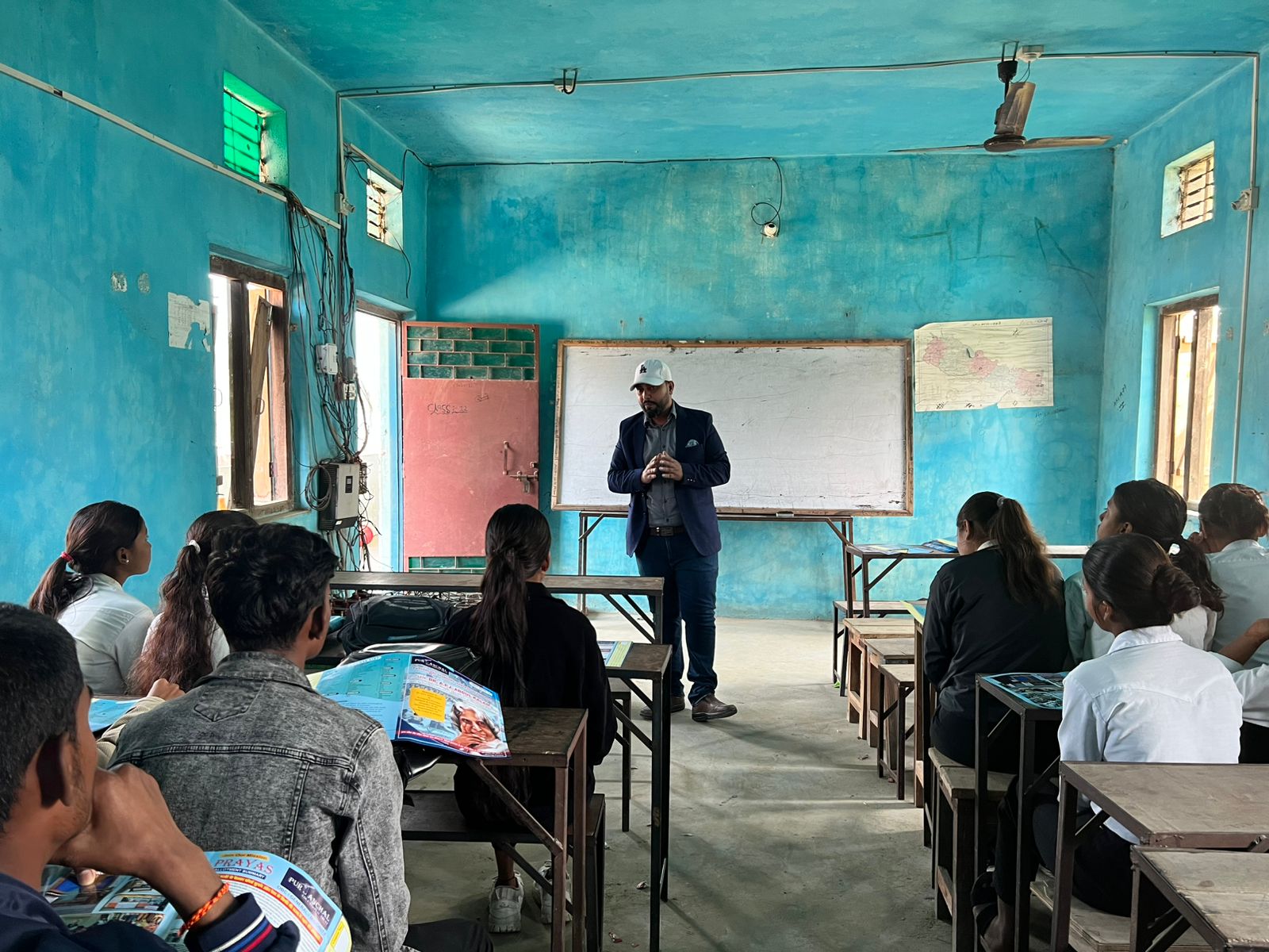 Mentor speaking to attentive students in a teal-walled classroom