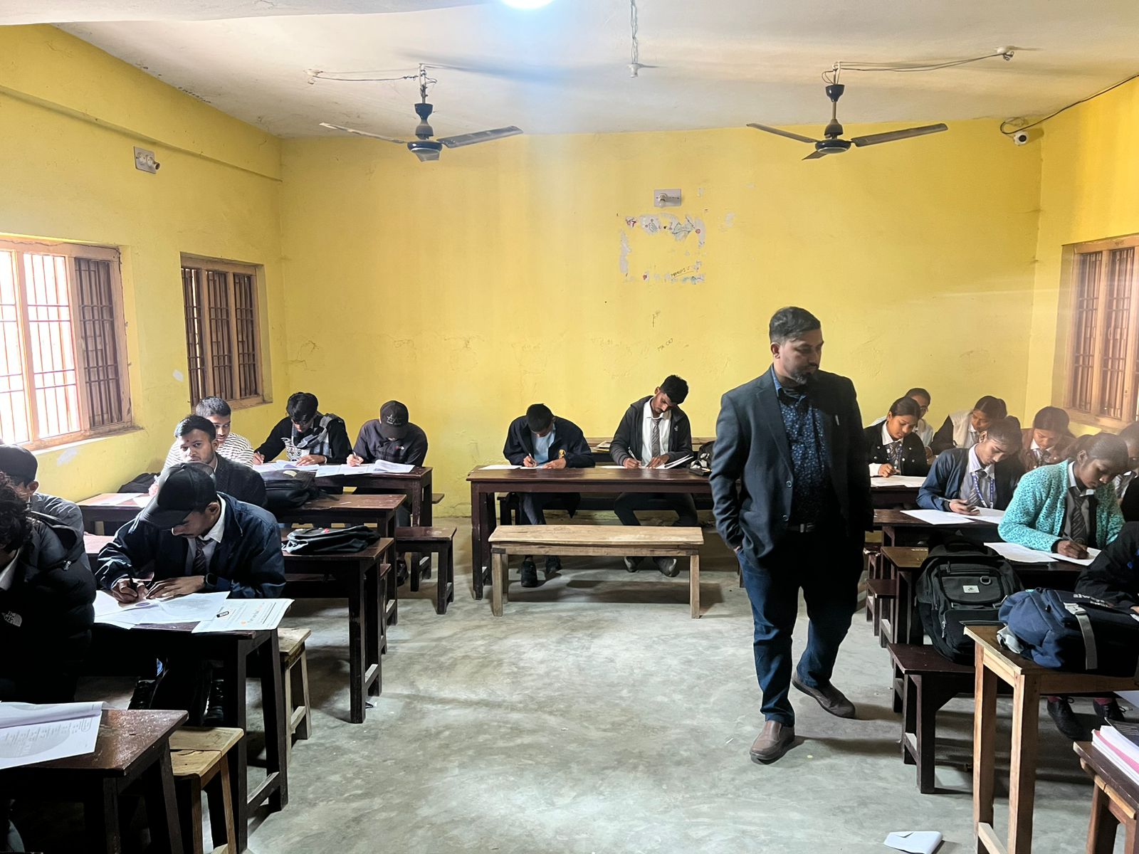 Students writing assessment papers in a yellow-walled classroom